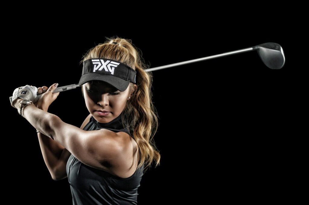 Golfer holding a driver across her shoulders against black