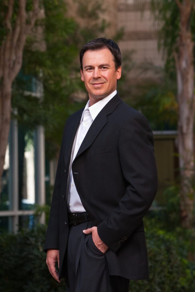 Man in a dark suit standing in a landscaped courtyard
