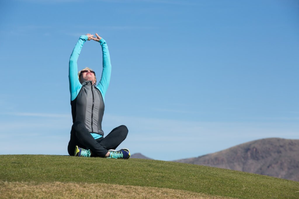 Woman seated outdoors with her arms stretched overhead