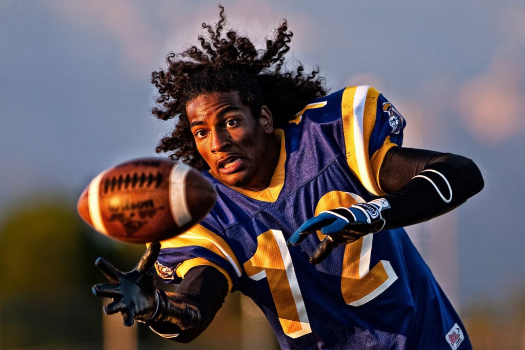 Football player with flowing hair reaching for a catch