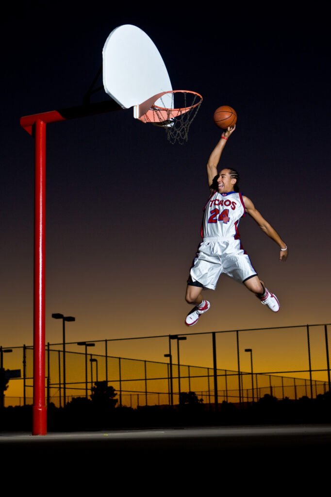 Basketball player reaching toward an outdoor hoop at sunset