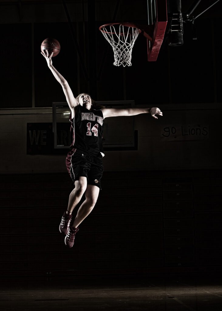 Basketball player airborne beside a hoop in a dark gym