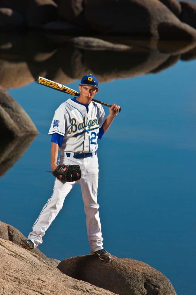 Baseball player holding a bat across his shoulders beside a lake